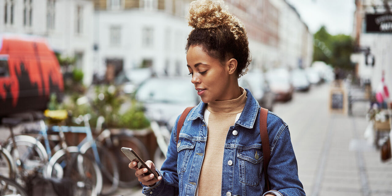 Una giovane donna è ritratta mentre è in una città con il suo smartphone in mano.